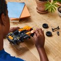 Kind bouwt een oranje en zwarte LEGO Technic NEOM McLaren Extreme E Team auto op een houten tafel.