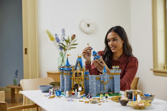 Een vrouw bouwt het LEGO Disney Kasteel, ze houdt een toren-onderdeel vast, klaar om te plaatsen.