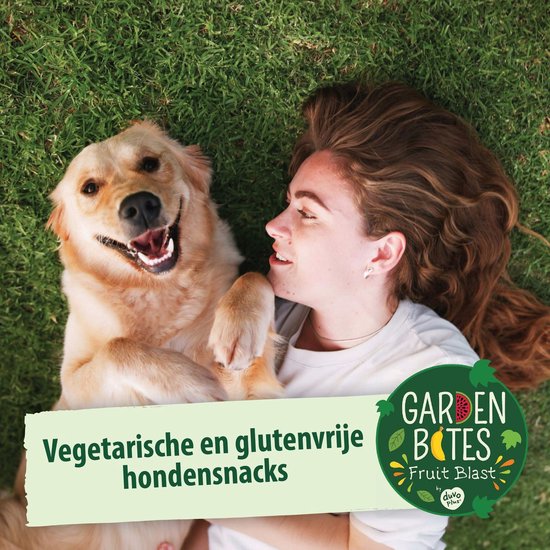 Een Golden Retriever ligt op zijn rug op gras naast een vrouw. Een vrouw lacht naar de hond. De hond is met zijn poten omhoog. Er is een Garden Bites logo.