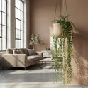 Kunst hangplant met parelkettingbladeren in een lichte pot, hangend in een woonkamer met grote ramen.
