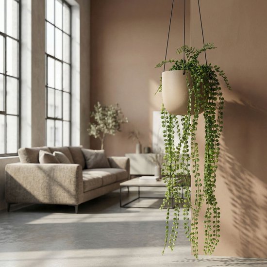 Kunst hangplant met parelkettingbladeren in een lichte pot, hangend in een woonkamer met grote ramen.