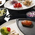 Detailopname van een stuk vlees dat wordt gegrild op een gourmetstel, met op het bord broccoli, tomaat, ui en champignons.