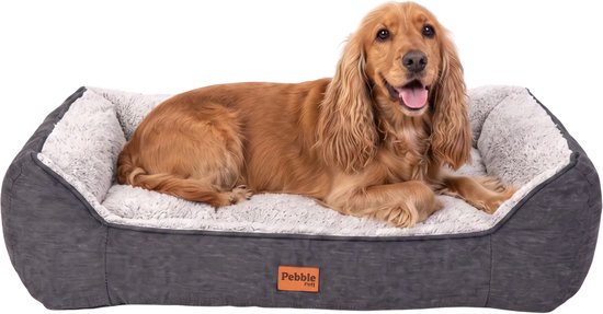 Un cocker spaniel repose dans un panier à chien gris avec une doublure intérieure blanche et douce. Le lit arbore une étiquette Pebble.