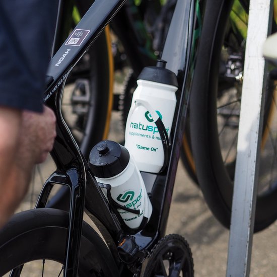 Zwarte racefiets met twee witte Natusport bidons in houders, gemerkt met 'Game On'.