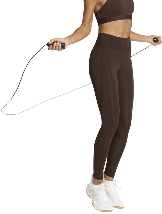 Model in bruine sportlegging en top springt touwtje, draagt witte sneakers.