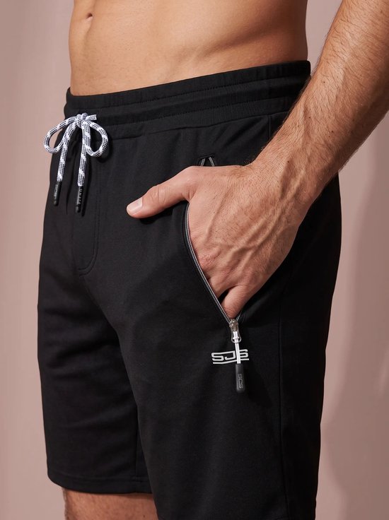 Zwarte sportshort met ritszak en wit Sjeng-logo, gedragen door een man.