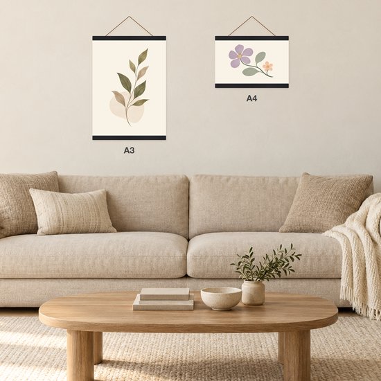 Interieur met een bank, houten tafel en twee posterhangers aan de muur met bladeren (A3) en bloemen (A4).