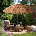 Raffia parasol bij een houten salontafel en rotan stoel op een terras.