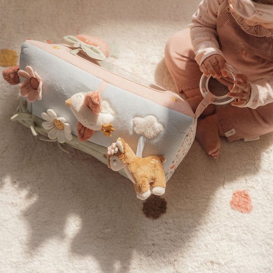 Zicht op de zijkant van de speelgoed driehoek met dieren en bloemen. Babyhandjes houden ring vast.