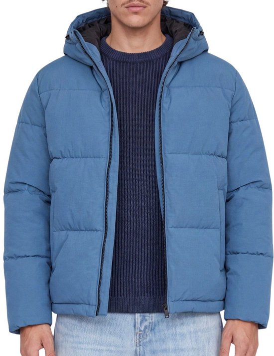 Blauwe pufferjas met capuchon, gedragen door een man met een blauwe trui en spijkerbroek.