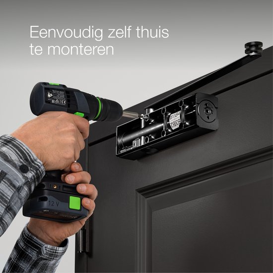 Man gebruikt een boormachine om een zwarte deurdranger op een zwarte deur te monteren.