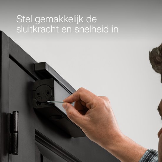 Man stelt de sluitkracht en snelheid in van een zwarte deurdranger met een inbussleutel.