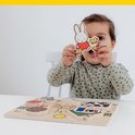 Een meisje met bruine krulletjes houdt een Miffy-puzzelstukje met kuikentjes omhoog, met een boerderijpuzzel op tafel.