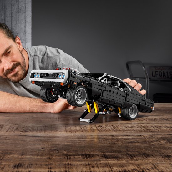 Een man tilt een zwarte Lego Charger op een krik.