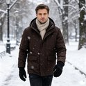 Man in bruine jas en beige sjaal draagt zwarte handschoenen en loopt door een besneeuwd park.