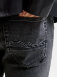 Close-up van de achterzak van een grijze jeans met witte stikseldetails.