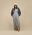 Model draagt een blauw sherpa jack, grijze jumpsuit, beige UGG-pet en bruine suède Lowmel-sneakers.