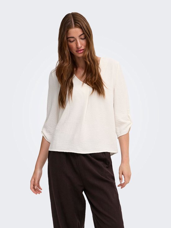 Model draagt een witte blouse met V-hals en donkerbruine wijde broek.