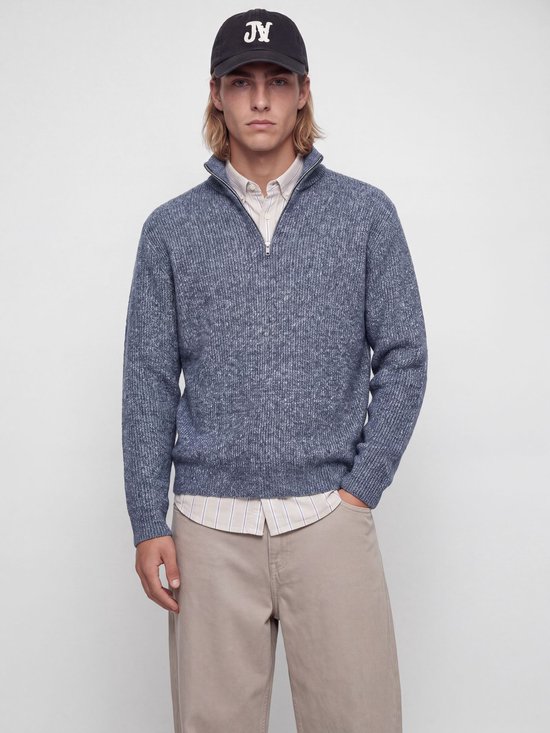 Model draagt blauwe gemêleerde gebreide polo met halve rits, gestreept overhemd, beige broek en pet.