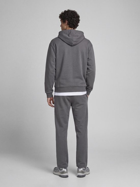 Model op de rug gezien, draagt een antracietgrijze hoodie, bijpassende joggingbroek en witte sneaker.