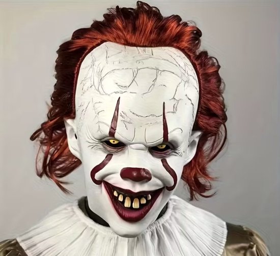 Close-up van Pennywise horrorclownmasker met oranje haar, wit gebarsten gezicht, gele ogen en angstaanjagende grijns.
