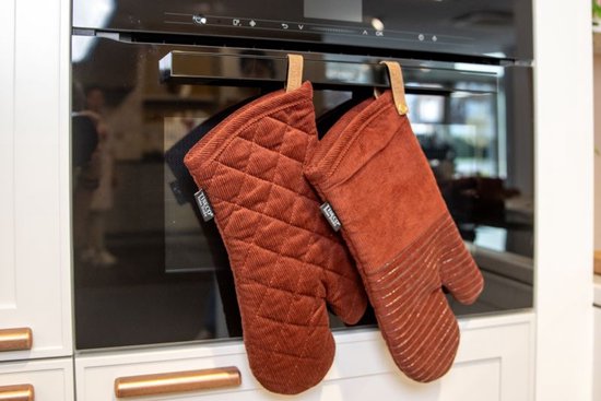Twee bruine Tiseco ovenwanten van ribstof hangen aan een ovenhandgreep, één met ruitpatroon en één met siliconen strepen.