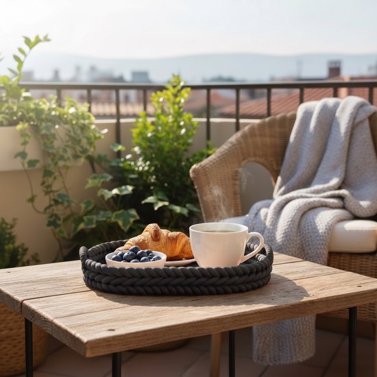 Zwart ovaal dienblad op balkon met croissant, blauwe bessen en koffie.