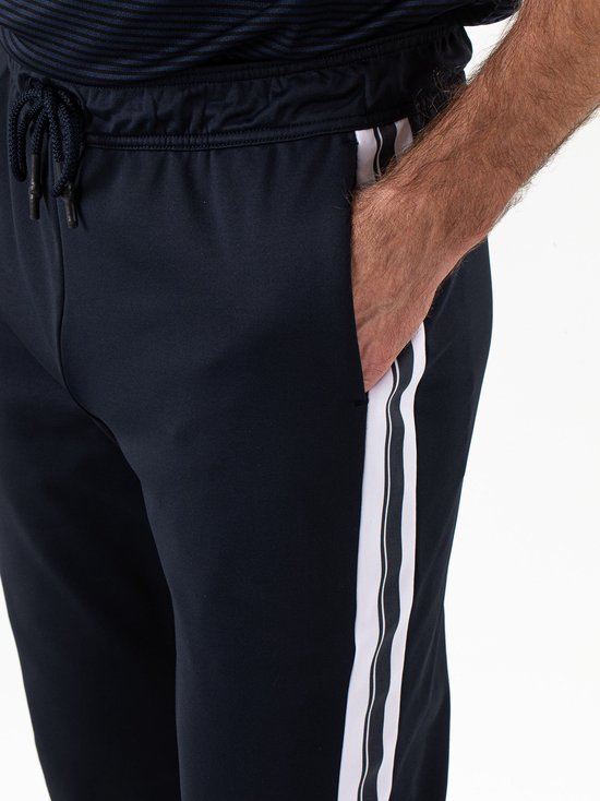 Close-up van de taille en zijzak van een donkerblauwe sportbroek met witte bies en trekkoord.