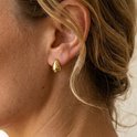 Close-up van een gouden druppelvormige oorknopje gedragen door een vrouw met blond haar.