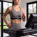 Vrouw met een VirtuFit hartslagmeter om haar borst, gekleed in sportkleding, traint op een loopband.