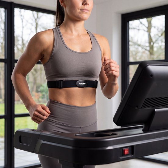 Vrouw met een VirtuFit hartslagmeter om haar borst, gekleed in sportkleding, traint op een loopband.