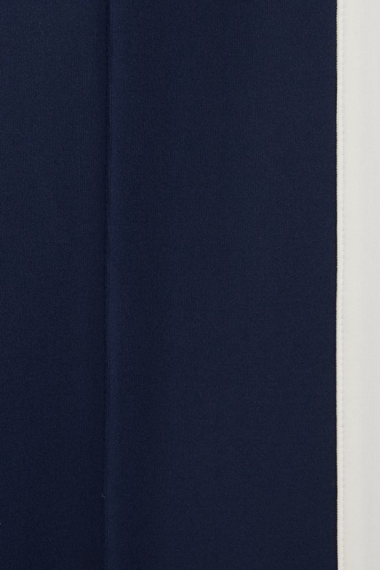 Detailopname van een donkerblauwe broek met een witte bies aan de zijkant.
