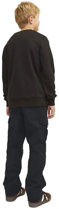 Jongensmodel in zwarte cargo broek, zwarte trui, bruine sneakers met strepen, zicht van achteren.