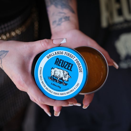 Handen houden een geopend blauw Reuzel pomade blik vast, 95g.