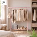 Roze kledingrek in een slaapkamer gevuld met beige kleding, een tas, een opbergdoos en schoenen op een houten vloer.