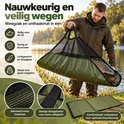Visser houdt olijfgroene weegzak met vis boven het gras; set met weegzak en mat.