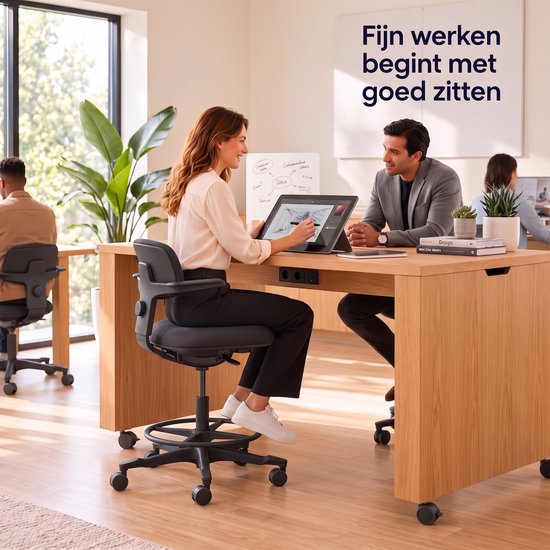 Een vrouw in een witte blouse en zwarte broek zit op een zwarte bureaukruk aan een houten bureau. Ze tekent op een tablet. Naast haar zit een man in een grijs pak. Er staat "Fijn werken begint met goed zitten" op de muur.
