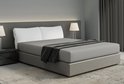 Un lit deux places avec un drap-housse gris, des oreillers blancs, un plaid gris foncé et des lampes de chaque côté.