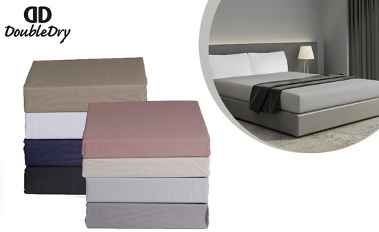 Pile de draps-housse taupe, blanc, bleu marine, vieux rose, beige et gris. En arrière-plan, un lit fait avec un drap gris.