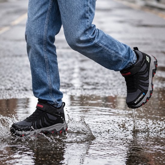 Zwarte Skechers Waterproof veterschoenen met rood accent en klittenband, gedragen met jeans in een plas.