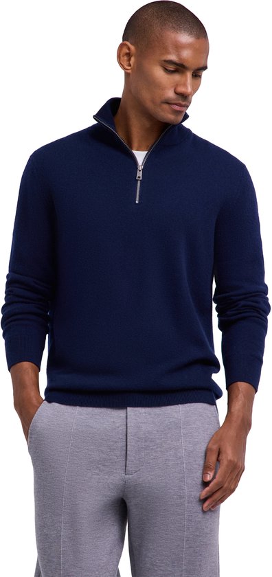 Model draagt een donkerblauwe FALKE trui met halve rits en een grijze broek.
