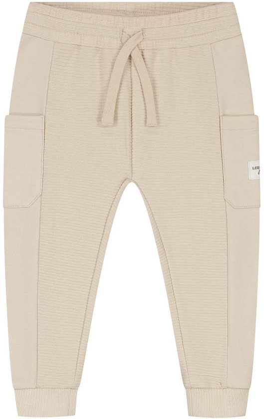 Crèmekleurige joggingbroek voor peuters met trekkoord, geribbelde stof en cargo zakken. Tekst op zak: 'LEGEND u'.