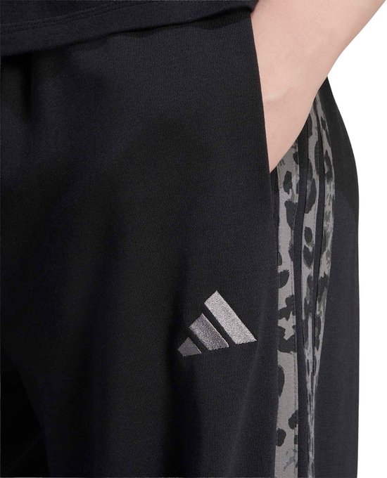 Close-up van het grijze adidas-logo op een zwarte joggingbroek met een luipaardprint detail.