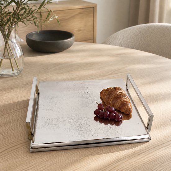 Een vierkant, zilverkleurig dienblad met handgrepen, met daarop een croissant en druiven.
