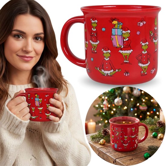 Vrouw houdt rode Grinch-mok met kerstmotieven vast bij een verlichte kerstboom.