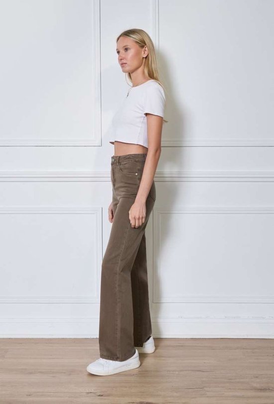 Model draagt een taupekleurige broek met straight fit en witte sneakers van opzij.