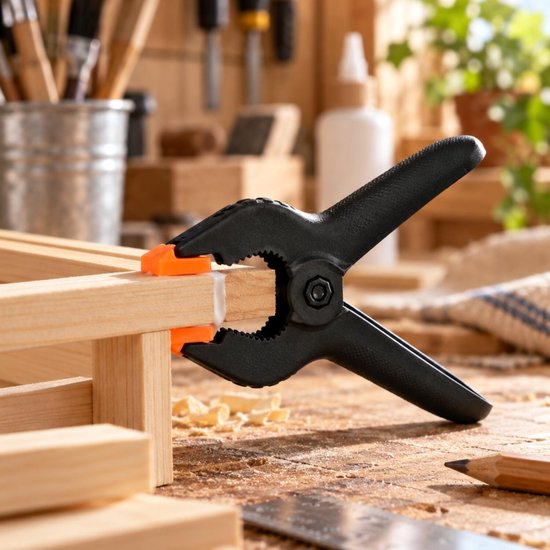 Zwarte veerklem met oranje bekleding klemt twee stukken hout samen op een werkbank met schaafsel.