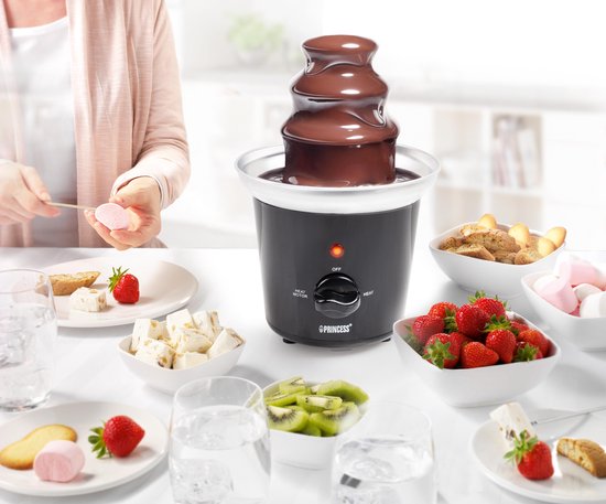 Zwarte Princess chocoladefontein met 3 lagen, omringd door fruit, marshmallows en koekjes. Een vrouw dipt een marshmallow.