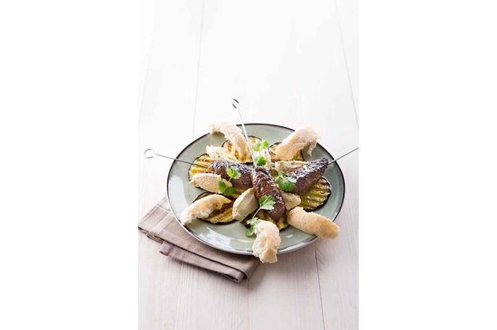 Een bord met spiesjes met vlees, aubergine en brood op een servet.
