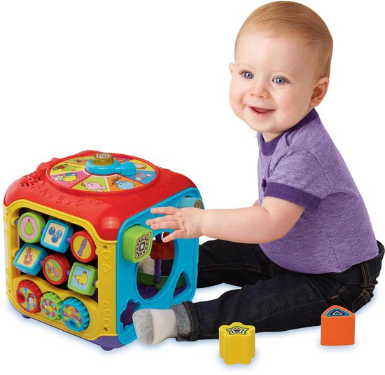 Een baby in een paars T-shirt speelt met een veelkleurige VTech activiteitenkubus met dierengeluiden en knoppen.